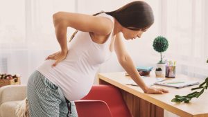 زن باردار که درد کمر ناشی از بارداری دارد و به میز خانه تکیه داده است